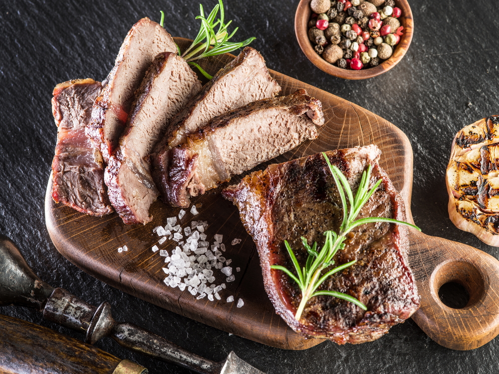 Carne bien cocida en una tabla de madera y granos de sal
