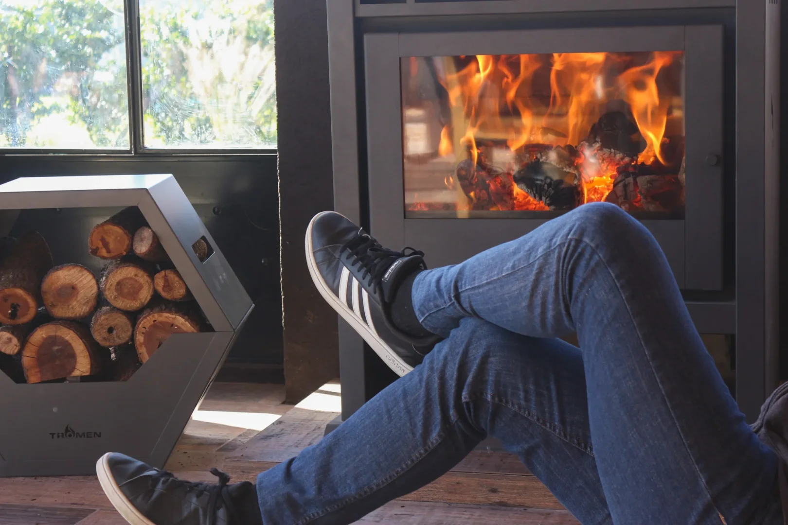 The legs of a person next to a Tromen salamandra and a pile of firewood.