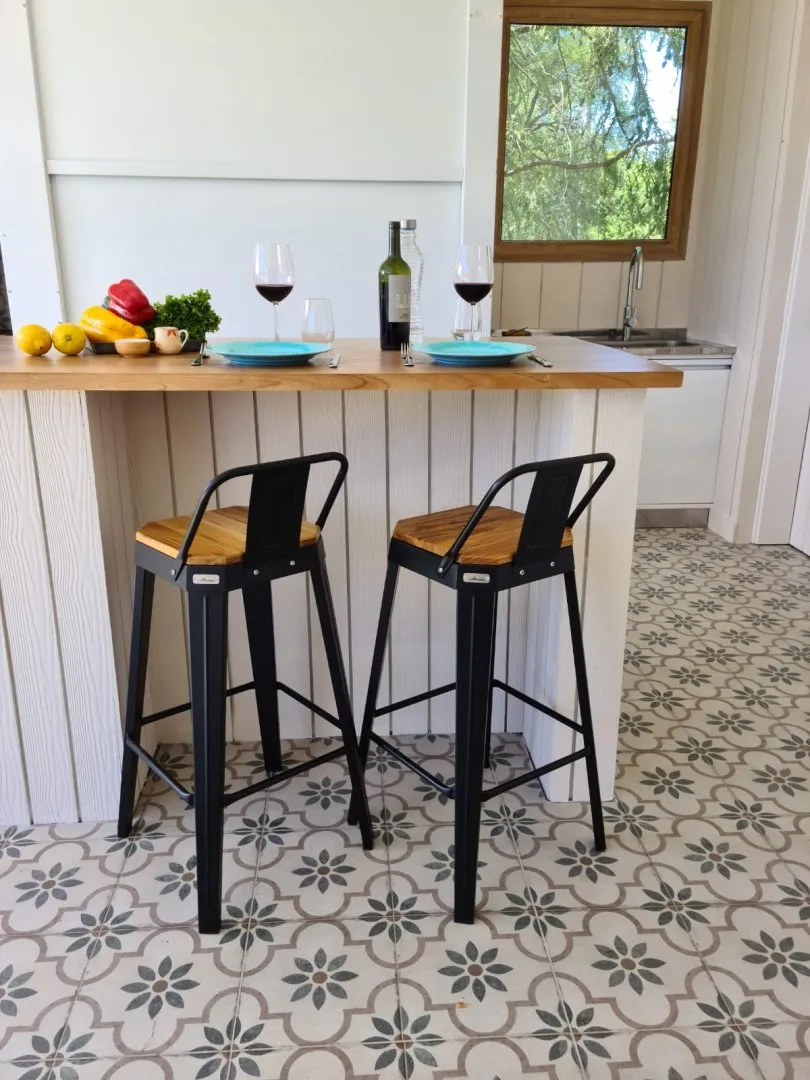 Dos banquetas de madera en un desayunador con platos, verduras y copas de vino