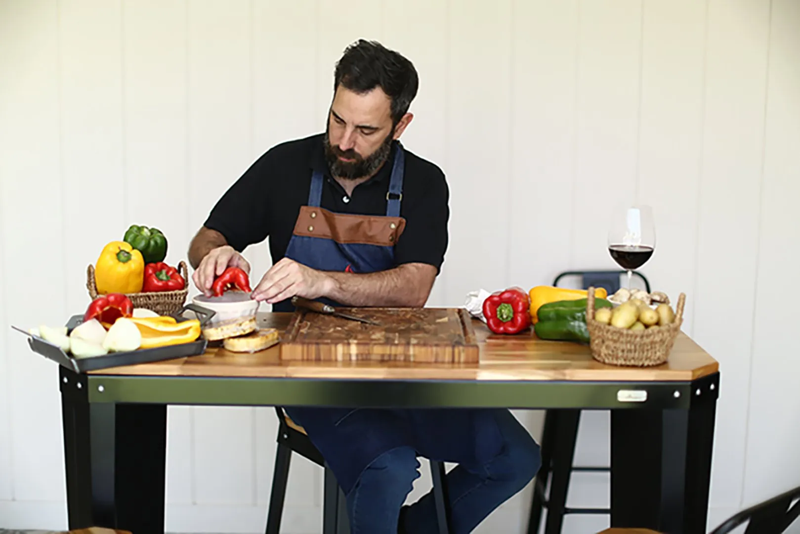 Un hombre cortando verduras en una tabla sobre una mesa de madera y metal.
