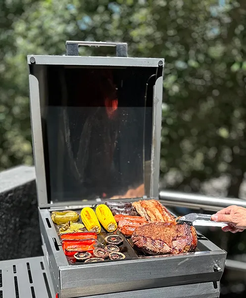 Grill with lid open and lots of vegetables and meat cooking