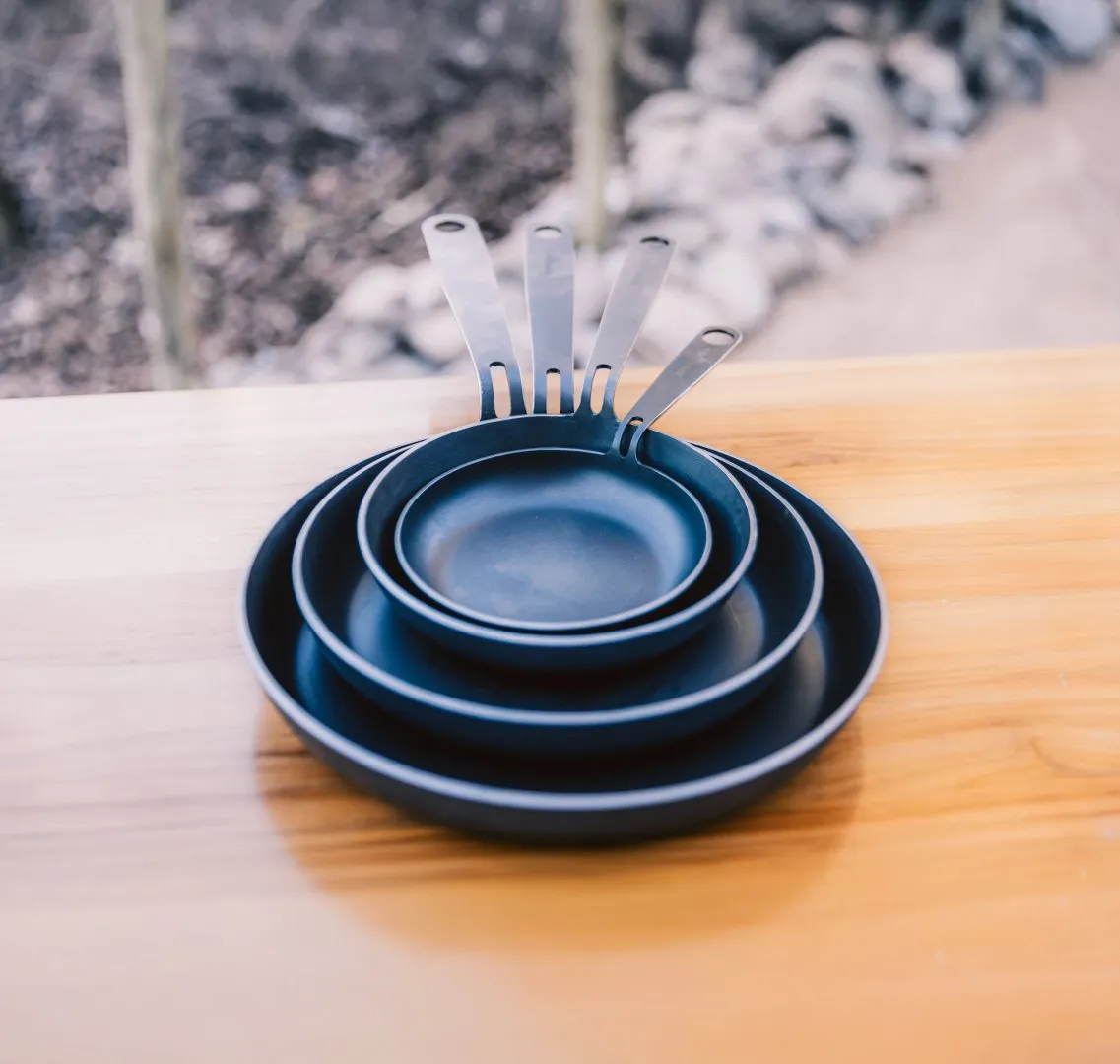 Steel frying pans of different sizes stacked on a table